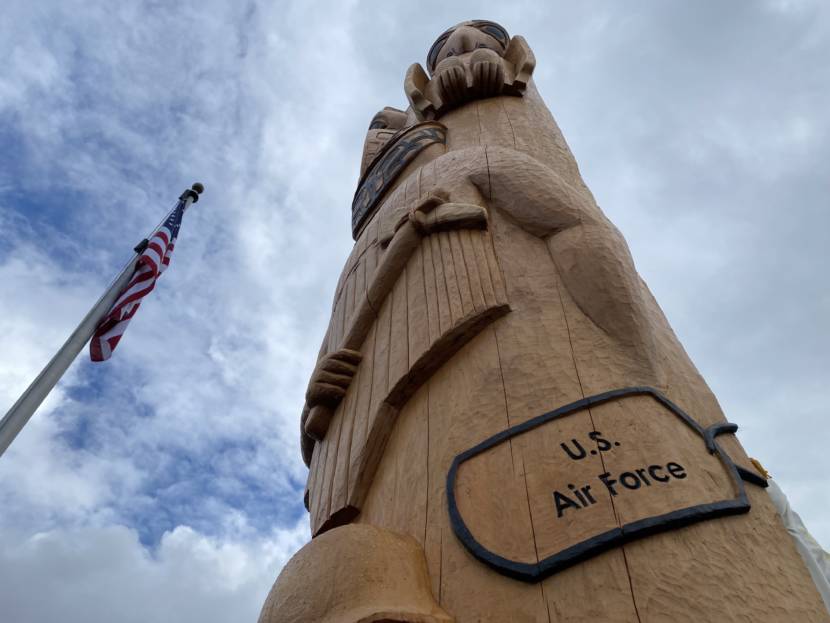 Toward the middle of the totem pole are carved dog tags representing each branch of the service, including the Alaska Territorial Guard, and a Tlingit warrior dressed in armor. 