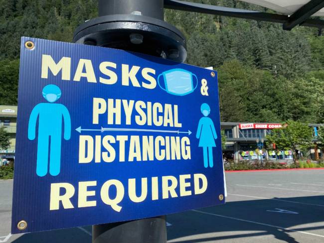 A blue sign with off white lettering that says: "Masks & physical distancing required" in all capital letters.