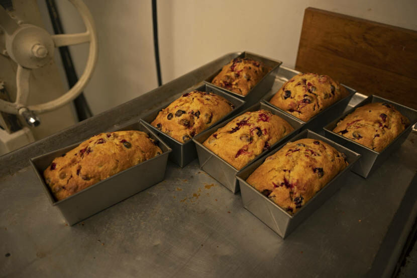 Seven freshly baked loaves of break sitting in their pans on a stainless steel table