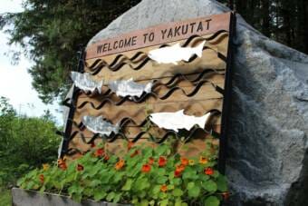A wooden sign with metal fish on it that says Welcome to Yakutat