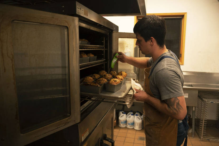 A baker standing at a large oven, checking loaves of bread