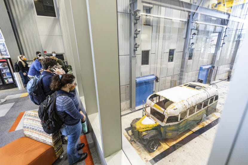 Students looking down on the Chris McCandless bus in a high-ceilinged vehicle bay