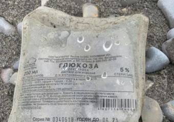An IV bag with Russian labelling lying on a beach