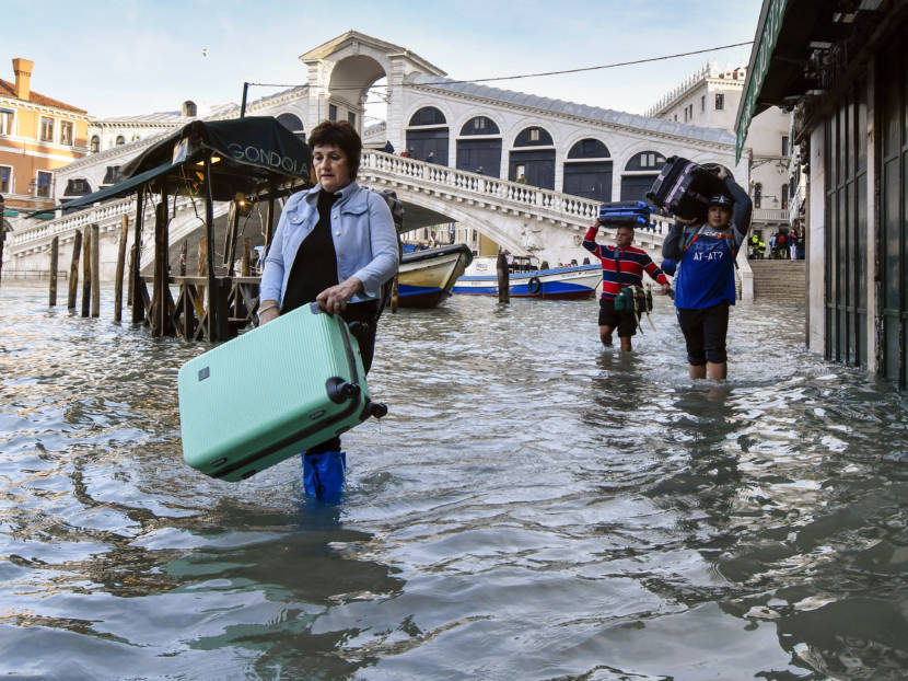 People wading through flooded Venice streets, carrying luggage