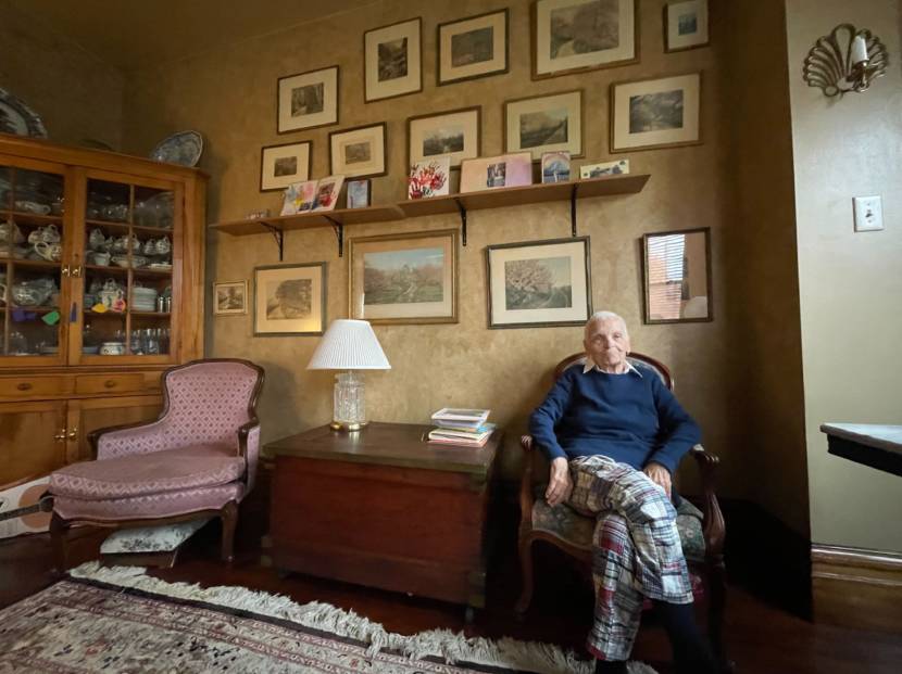 An elderly woman sitting in a room with many pictures on the wall