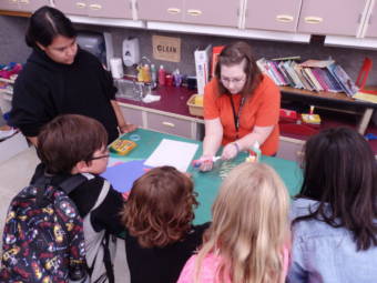 A photo taken from above showing a teacher and students around a table in a classroom