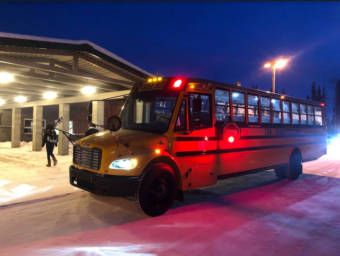 A school bus in front of a school on a dark Interior Alaska morning with snow on the ground