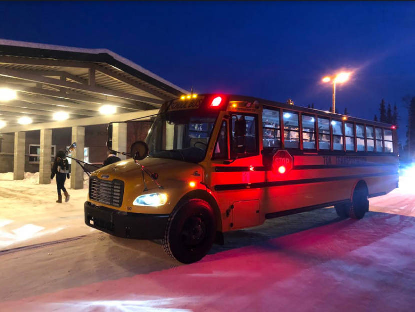 A school bus in front of a school on a dark Interior Alaska morning with snow on the ground