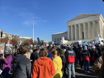 Protestors standing outside the U.S. Supreme Court building on a sunny day