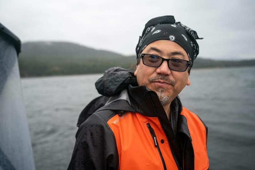 A man wearing a black bandana and an orange-and-black raincoat standing on a boat