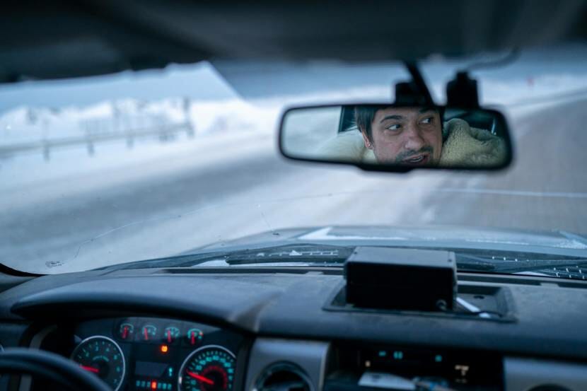 The face of a man seen in the rear-view mirror of the car he's driving on snowy roads