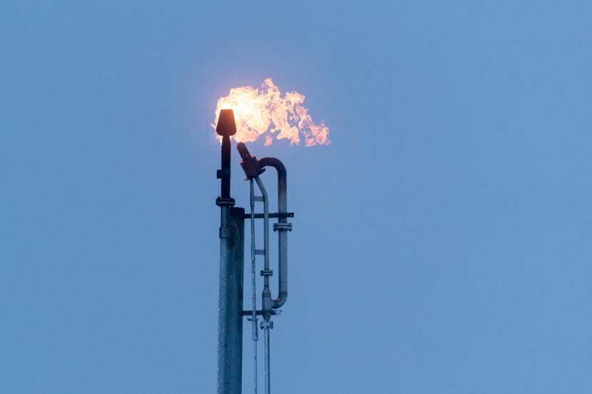 A natural gas stack with a flame at the top, with the sky in the background