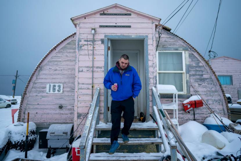 A man coming down the front steps of a pink quonset hut in winter