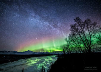 A heavily post-processed photo of a vividly green and red aurora over a river with Denali in the background