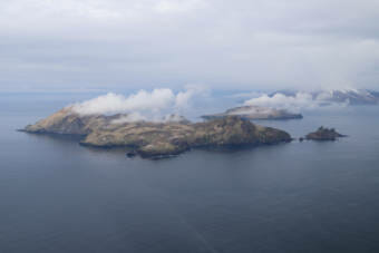 A group of small islands in the foreground with a larger, conical volcano behind them.