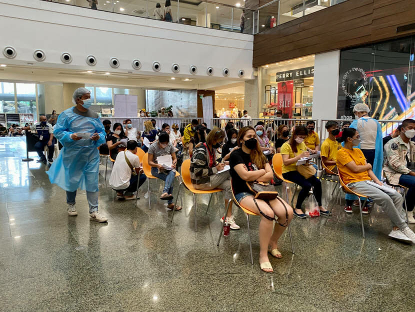 Masked people seated in rows of chairs, waiting to be vaccinated in a mall.