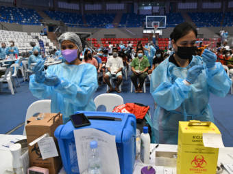 Two health workers in protective gear prepare to administer vaccines at a mass clinic in an arena