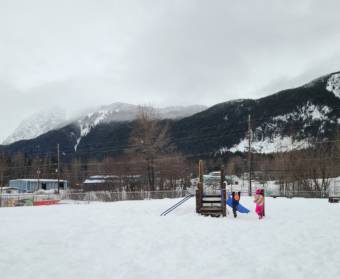 Children playing at a snowy playground with mountains in the background.