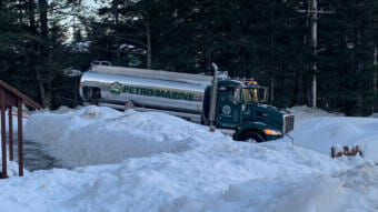 A fuel truck backed into a driveway surrounded by deep snow