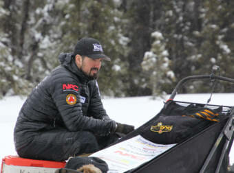 a man sitting on a cooler next to a dogsled