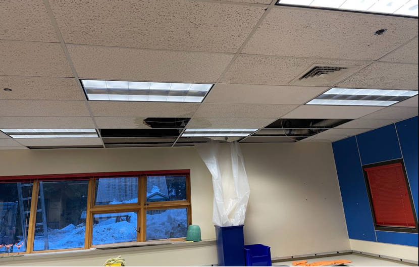 A classroom with ceiling tiles missing and a garbage can set up to catch leaking water