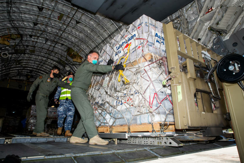 men in military uniforms unloading a pallet of supplies from a cargo plane