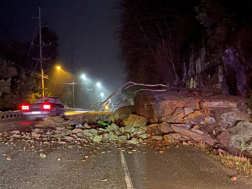 A nighttime photo of a car driving around a large pile of rocks that has fallen into the road