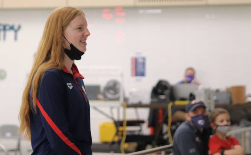 Lydia Jacoby standing poolside, talking to young swimmers