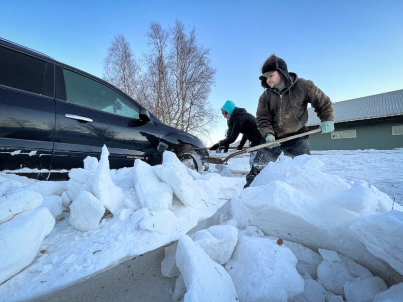 A man with a shovel, digging a truck out of deep snow