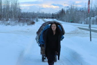 A woman pulls a cart filled with possessions down a snow-covered bike path