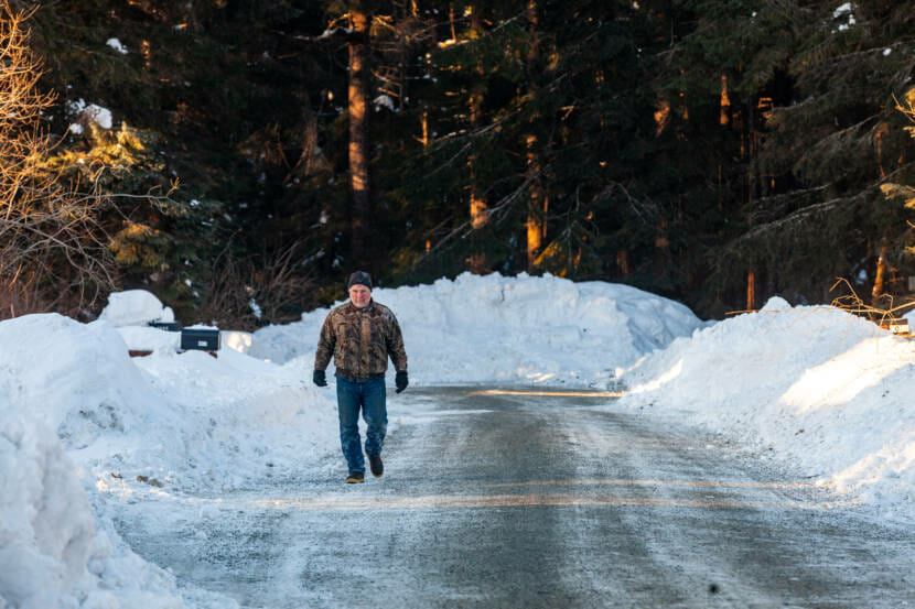 A man walks up a plowed street with deep snow banks on either side