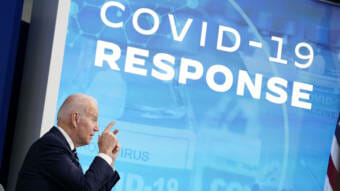 President Biden speaking in front of a projected graphic that says "COVID-19 response"