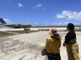 Two people watching a military cargo plane taxi from a runway
