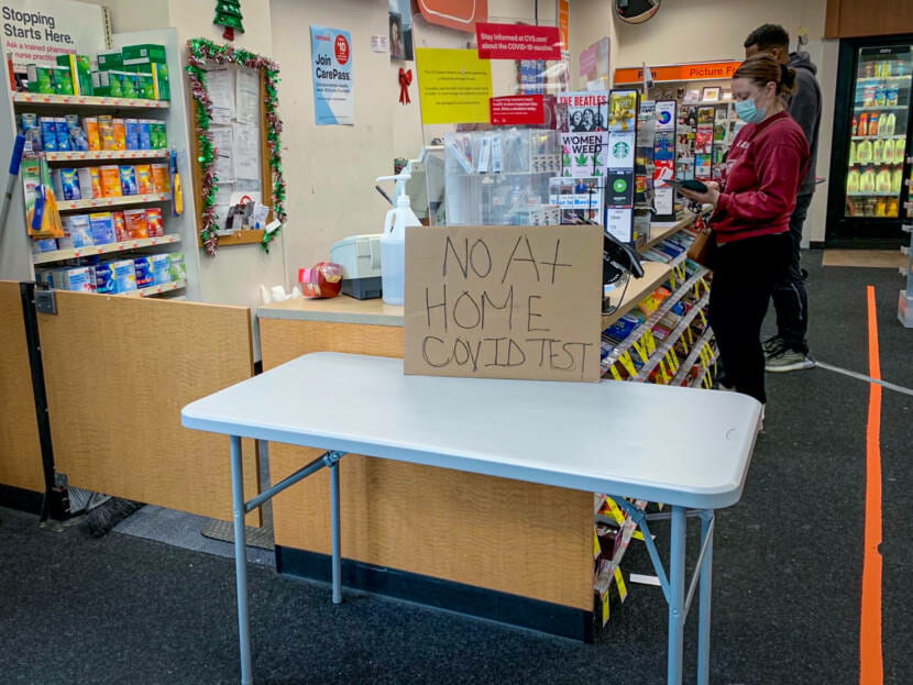 An empty table by a pharmacy checkout with a sign that says "no at-home covid test"