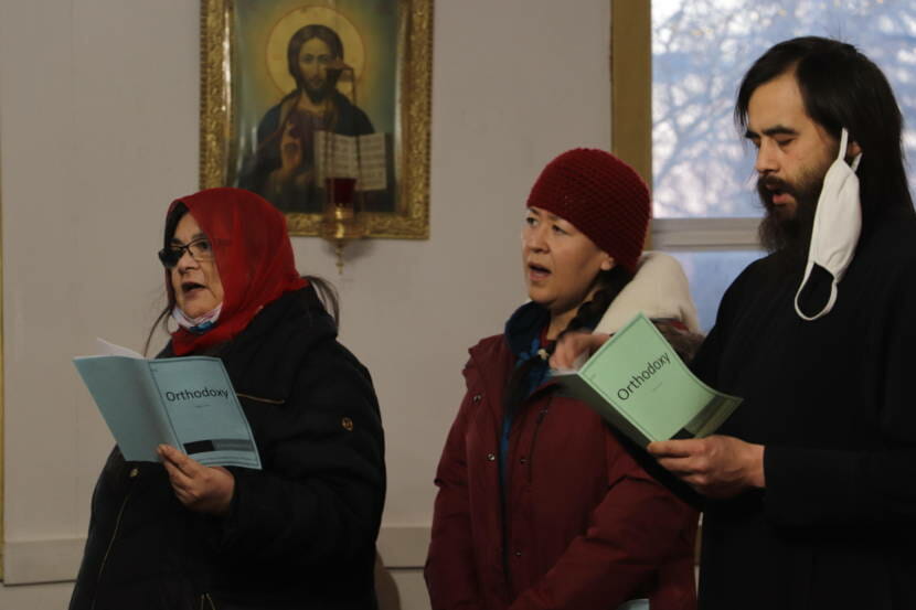 Three people dressed in winter clothes, singing inside a church