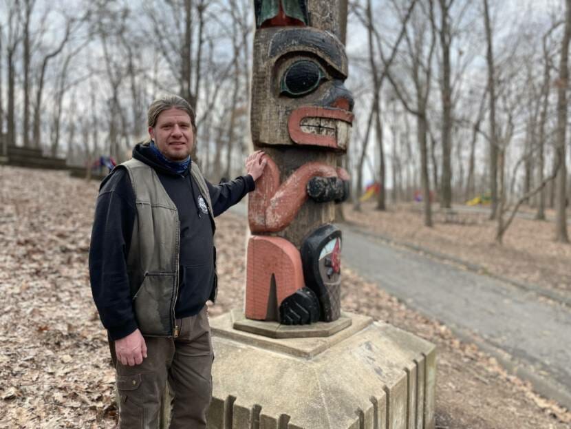 A man stands next to a totem pole by a suburban street