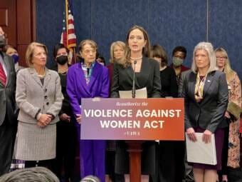 Angela Jolie standing at a lectern with a sign on it that says Violence Against Women Act