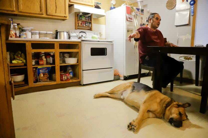 A man sitting at a kitchen table with a large dog lying on the floor next to him