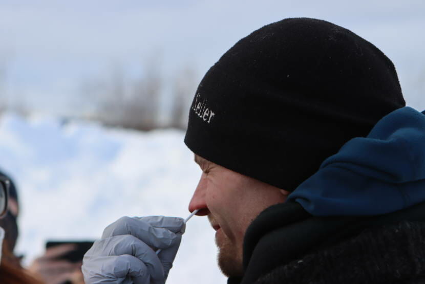 A man outside in winter gear with a gloved hand holding a nasal swab in his nose.