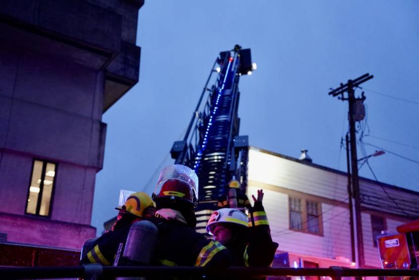 Three firefighters in front of a ladder truck with its ladder raised
