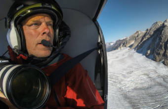 A man holding a camera in a helicopter flying over a glacier