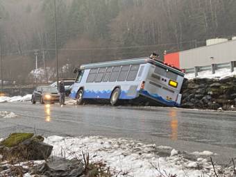 A city bus on a wet road, leaning heavily to its right with two wheels in the ditch