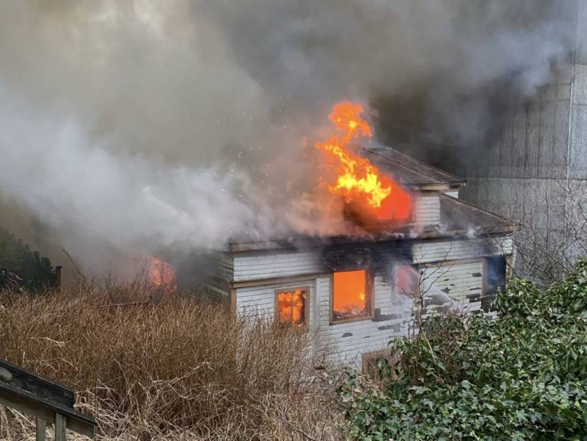 A white, wood-frame apartment building fully engulfed in flames