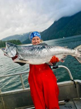 Seorang wanita di perahu nelayan memegang salmon raja yang sangat besar