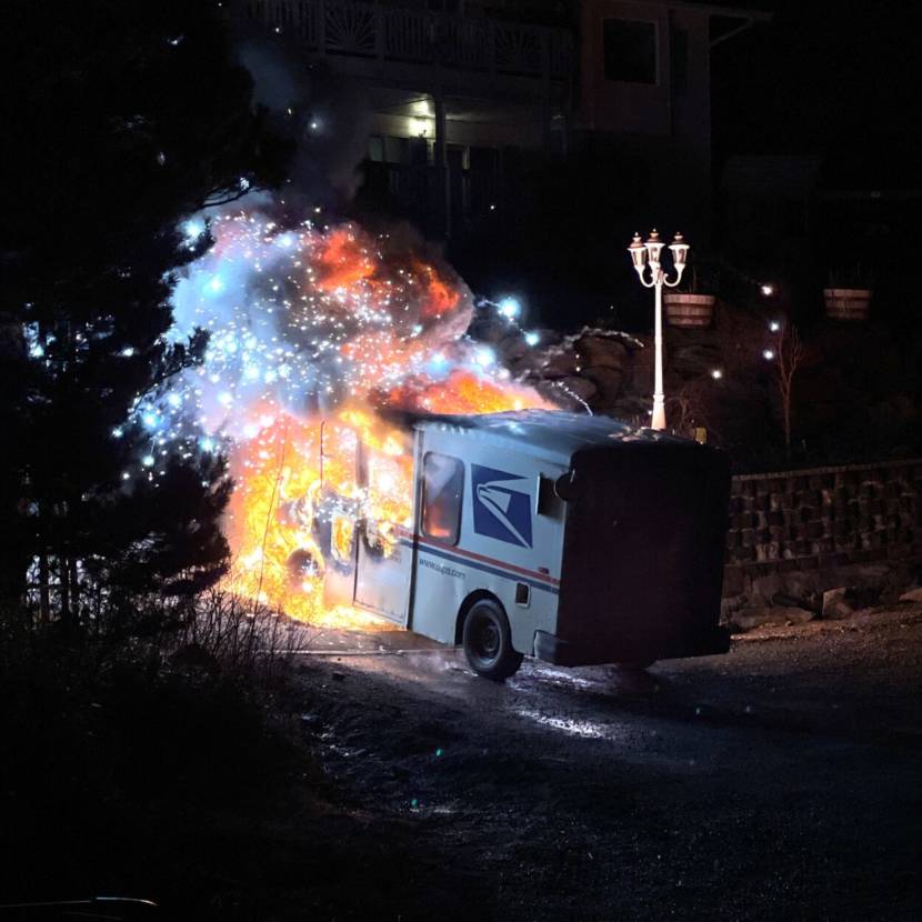 A mail truck in a dark driveway, its front half completely engulfed in a dazzling, sparkly ball of flames