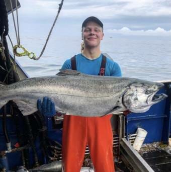 A man on a fishing boat holding a very large king salmon