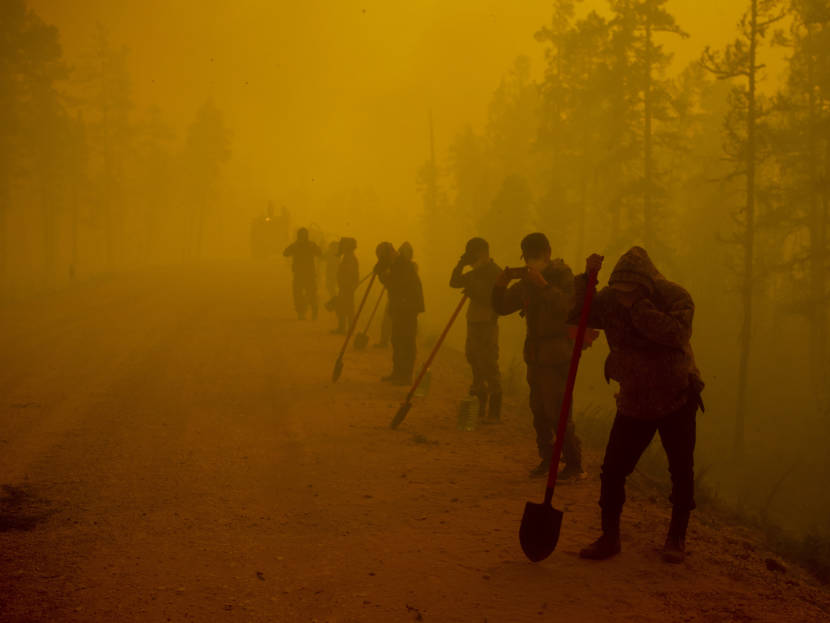 Wildland firefighters standing along a road among eerily red-brown smoke