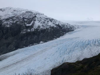 The tongue of a glacier with a mountain visible through fog in the background