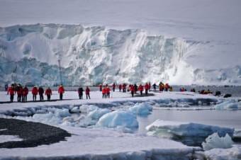 A large group of people in matching red parkas standing on an icy shore