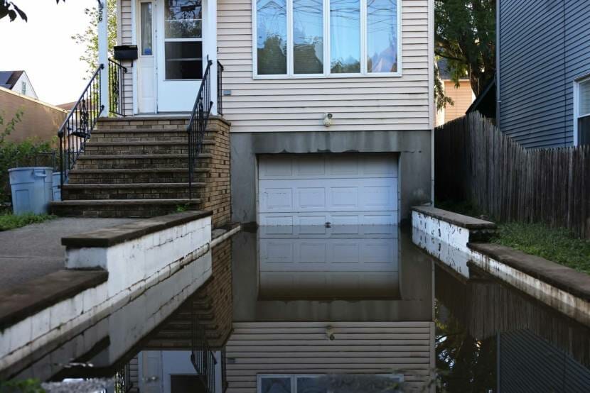 A small house with a basement garage; the driveway is flooded halfway up the height of the garage door